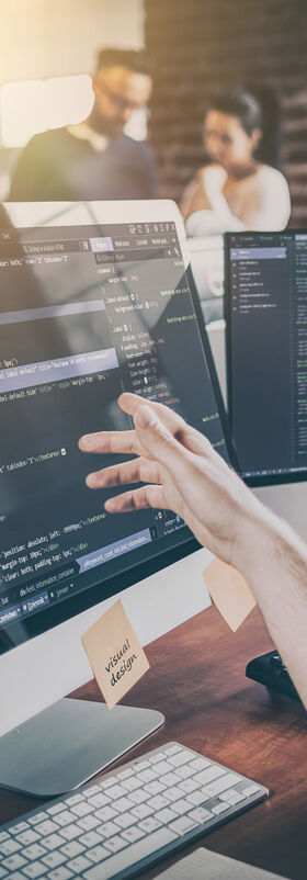 Security risks Employees in an office viewing source code on a screen to identify security risks using T Business solutions.