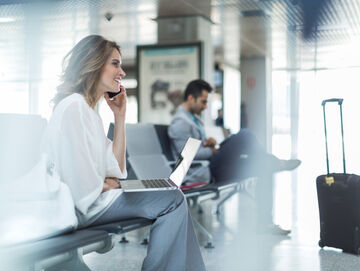 New work A woman working with her smartphone and laptop on an airport with new work solutions for digital workplaces by T Business.