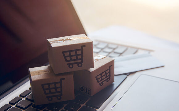 Paper cartons with a shopping cart logo on a laptop that's searching for logistics IT solutions