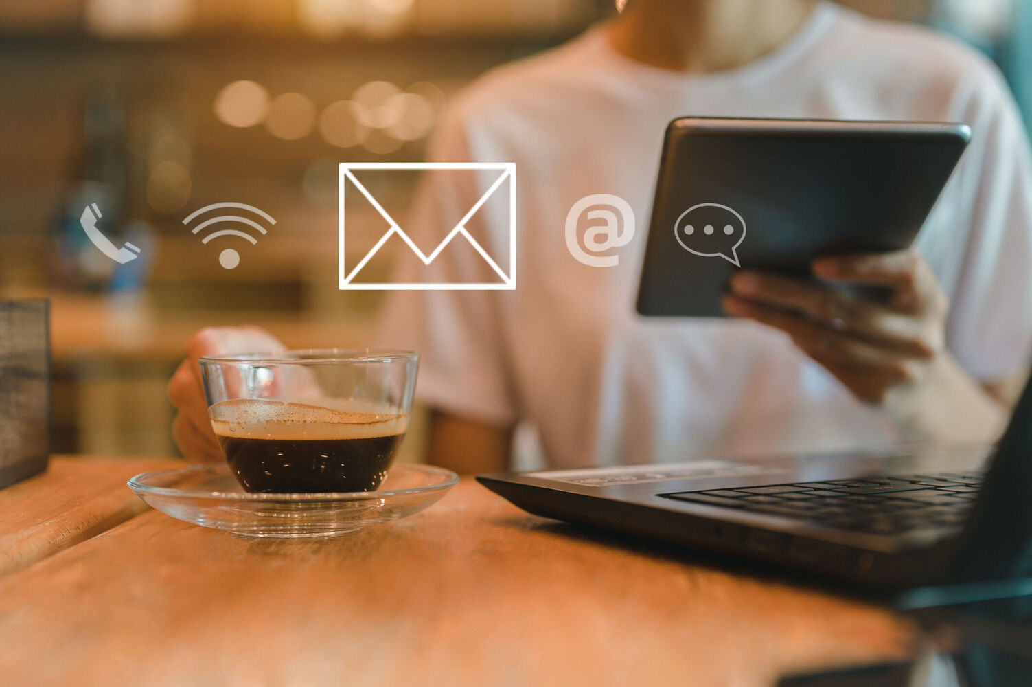A women sitting in a cafe with a laptop on the table, a coffee in one hand and holding tablet in the other hand, using wireless technology to work remotely.