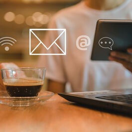 A women sitting in a cafe with a laptop on the table, a coffee in one hand and holding tablet in the other hand, using wireless technology to work remotely.