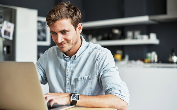 A young man using his laptop in his kitchen working for a SMB