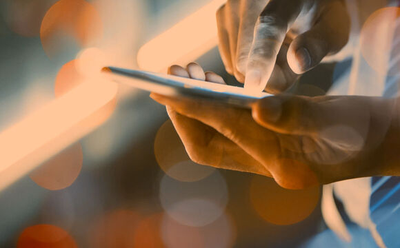 A person holding a smartphone in one hand and with the other typing on the mobile phone.