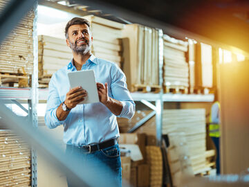 A man holding a tablet in a warehouse working with the next generation hybrid data center, T Business solution.