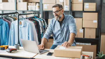 Online Marketing For Small Business A man standing in the storeroom of a shipping company is viewing the small company's online marketing on his laptop