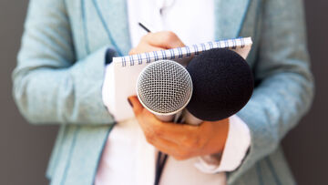 Security risks A woman holds a notebook and microphones, symbolizing the reports and recommendations you receive from T Business' IT health check to minimize security risks.