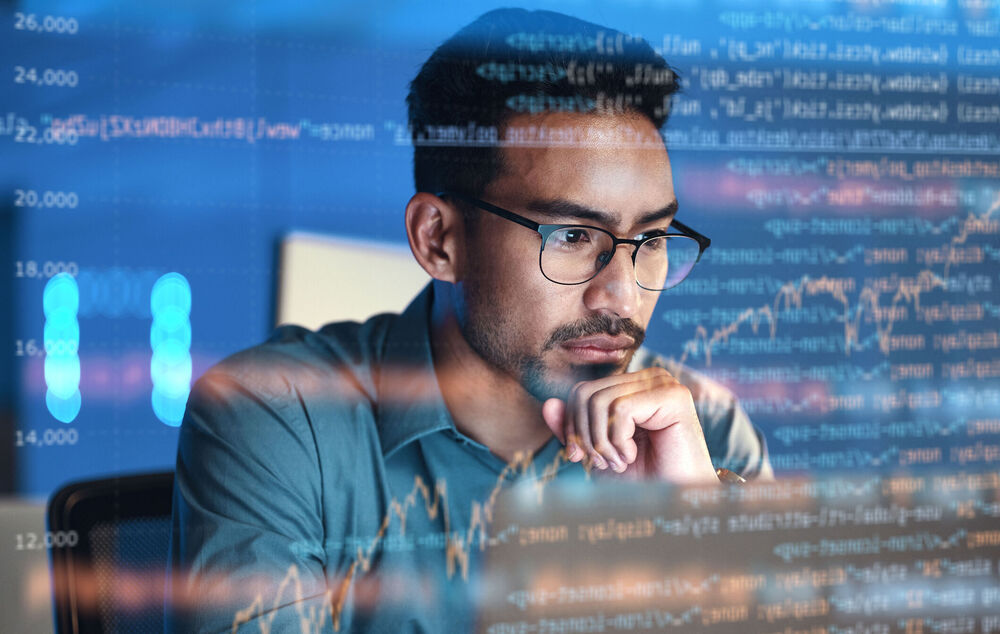 IT security A man with glasses out of view of a screen with various numbers on the display leans lightly on his hand and observes how NIS2 protects his systems and data.