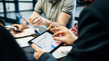 Secure Connectivity In a business meeting, numbers are analyzed on a tablet connected to a reliable network with secure connectivity services by T Business.