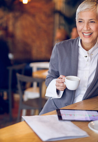 Senior businesswoman working on digital tablet in cafe while drinking coffee, using secure cloud solutions from T Business Europe.