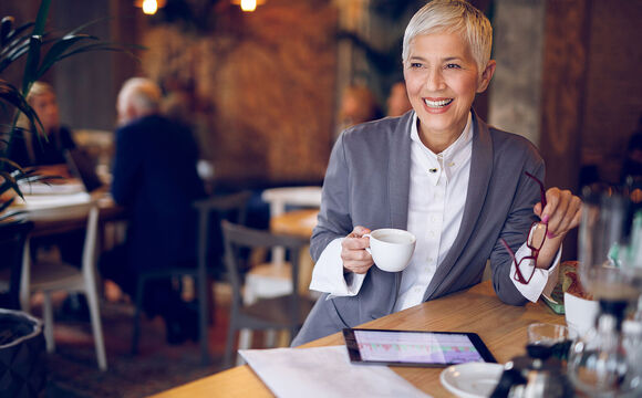 Senior businesswoman working on digital tablet in cafe while drinking coffee, using secure cloud solutions from T Business Europe.