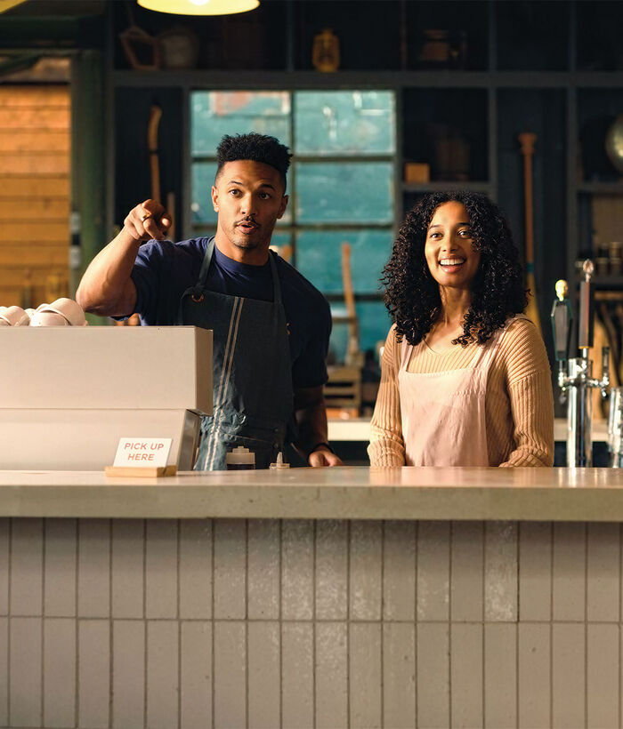 Fast Internet Connection A waitress and a waiter are standing behind a bar in a modern café, featuring a beer tap and a coffee machine.