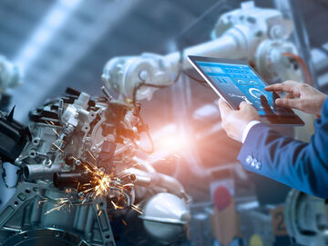 Engineer manager working on a robot arm, while searching banking and financial solutions on his tablet