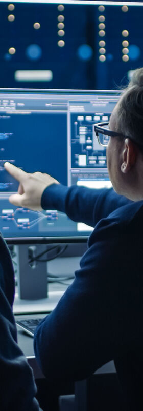 SOC Services - Security 27/7 Two professional IT employees working with SOC services from T Business on desktop computers.