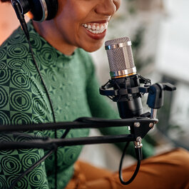 A woman sitting in front of a microphone and doing a podcast to the one from T Business and COSMOTE.