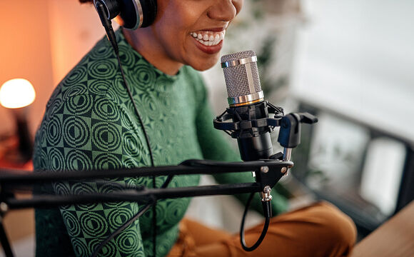 A woman sitting in front of a microphone and doing a podcast to the one from T Business and COSMOTE.