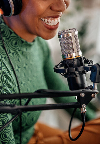 A woman sitting in front of a microphone and doing a podcast to the one from T Business and COSMOTE.