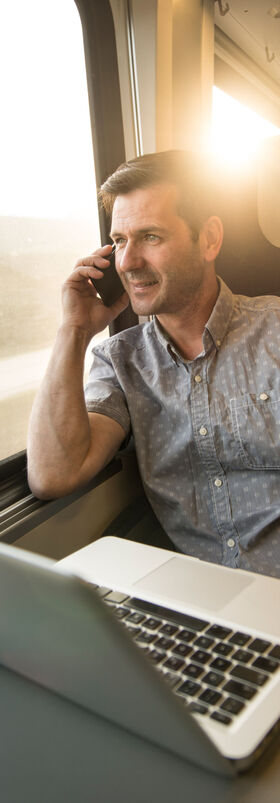 New work A man is on the phone on the train, a laptop is on the table in front of him and he is working with new work solutions for digital workplaces from T Business.