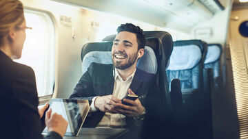 SD-X Two business professionals are working mobile in a train with a smartphone and laptop, securely connected with the SD-X solution by T Business.