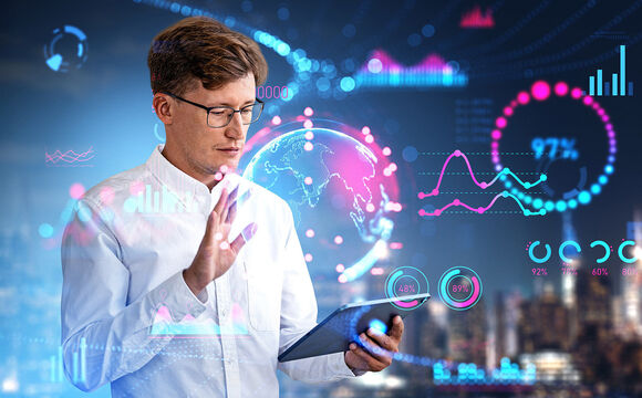 A man in a white shirt and glasses with a tablet in his left hand. With his right hand, he projects a fluorescent globe over the tablet and numerous other fluorescent numbers and statistics surround him.