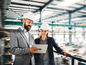 A man and a woman in a factory searching on their tablet for banking and financial solutions