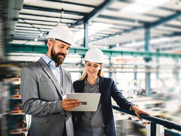 A man and a woman in a factory searching on their tablet for banking and financial solutions
