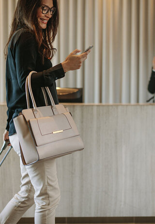 Digital Communication | T Busienss Woman using mobile phone to digitally check in via the communication platform from T Business Europe. The female business traveler walking in hotel hallway and pulling her suitcase.