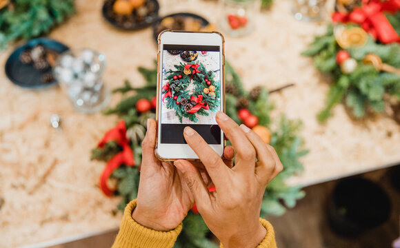 A florist taking a picture of a wreath on a smartphone for her flower shop, that works with digitalization | T Business