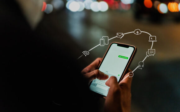 Silhouette of a person from behind, holding a smartphone and typing a message into a chat program. Icons float around the smartphone to illustrate the communication platform.