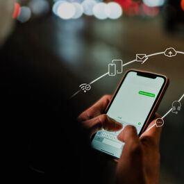 Silhouette of a person from behind, holding a smartphone and typing a message into a chat program. Icons float around the smartphone to illustrate the communication platform.