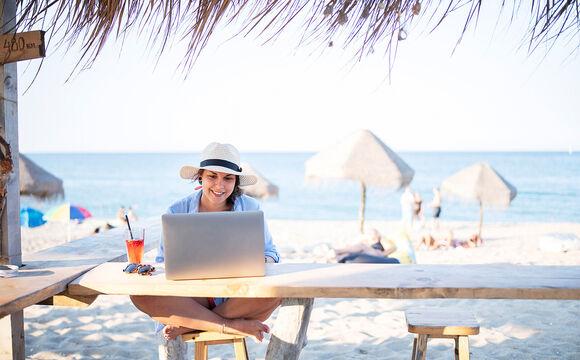 A woman sitting at a beach, while working remote