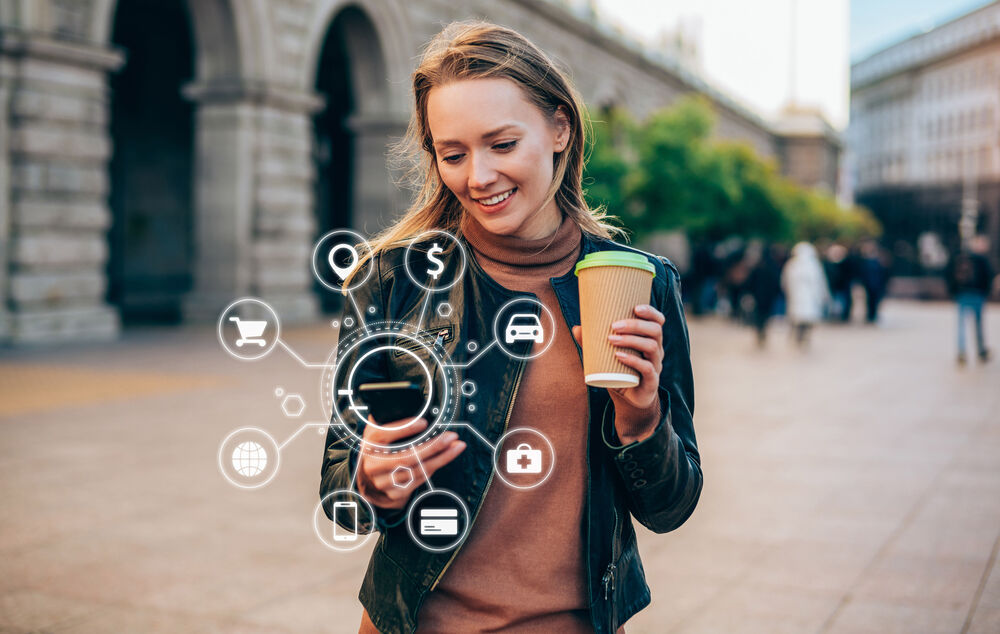 Connectivity solutions A woman in the city, cup of coffee in hand, does everything on the go with her smartphone using T Business connectivity solutions.