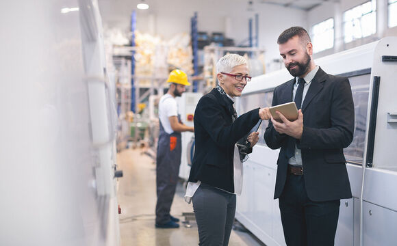 Workers in a factory looking for manufacturing IT solutions on their tablet