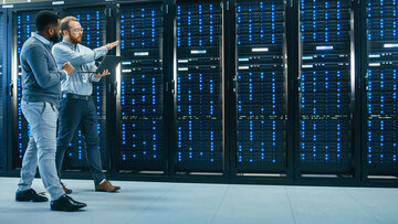 NIS2 Requirements Two men chatting and walking along racks in a data center.